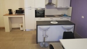 Una cocina compacta con armarios blancos, microondas, horno, lavabo y dos taburetes de bar.