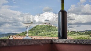 Una copa de vino y una botella en un balcón con vistas a un edificio en la cima de una colina.