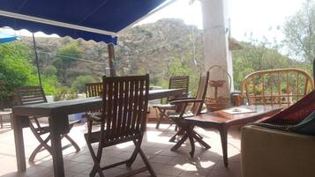 An outdoor patio with wooden furniture, a covered area, and a view of rocky terrain.