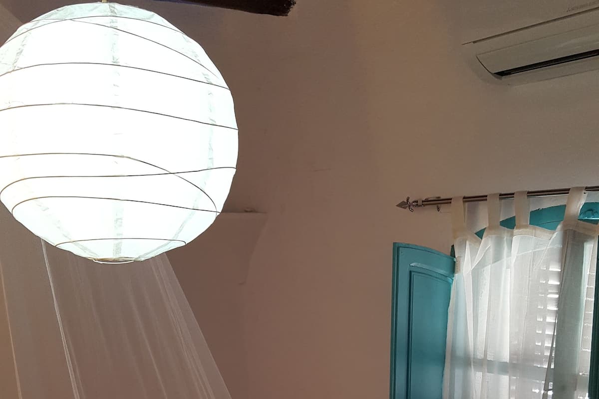 A bedroom with a bed, a canopy, a window with curtains, and a wall-mounted air conditioner.