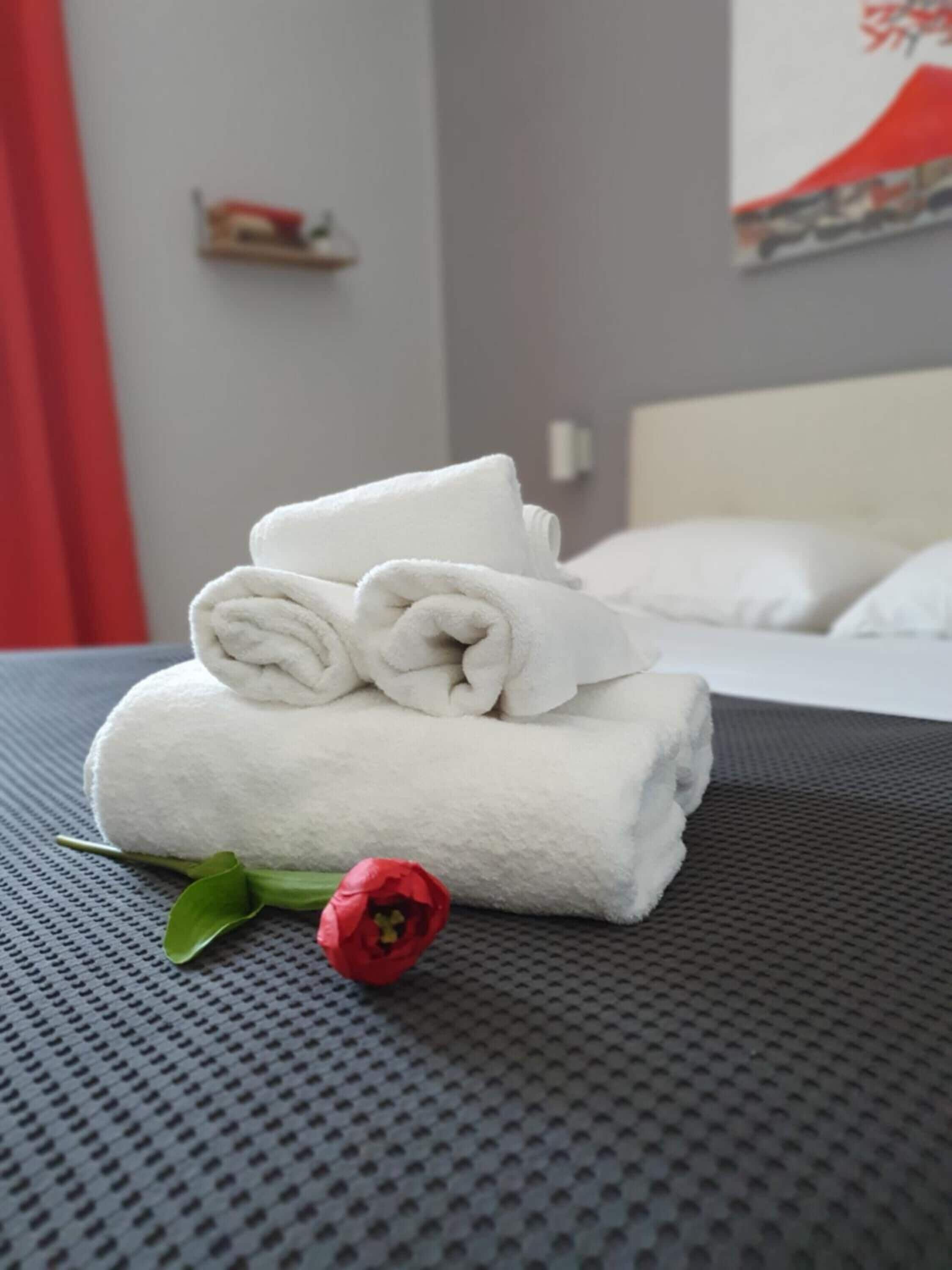 A neatly made bed with white towels and a red flower on a textured grey bedspread.