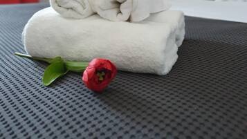 A neatly made bed with white towels and a red flower on a textured grey bedspread.