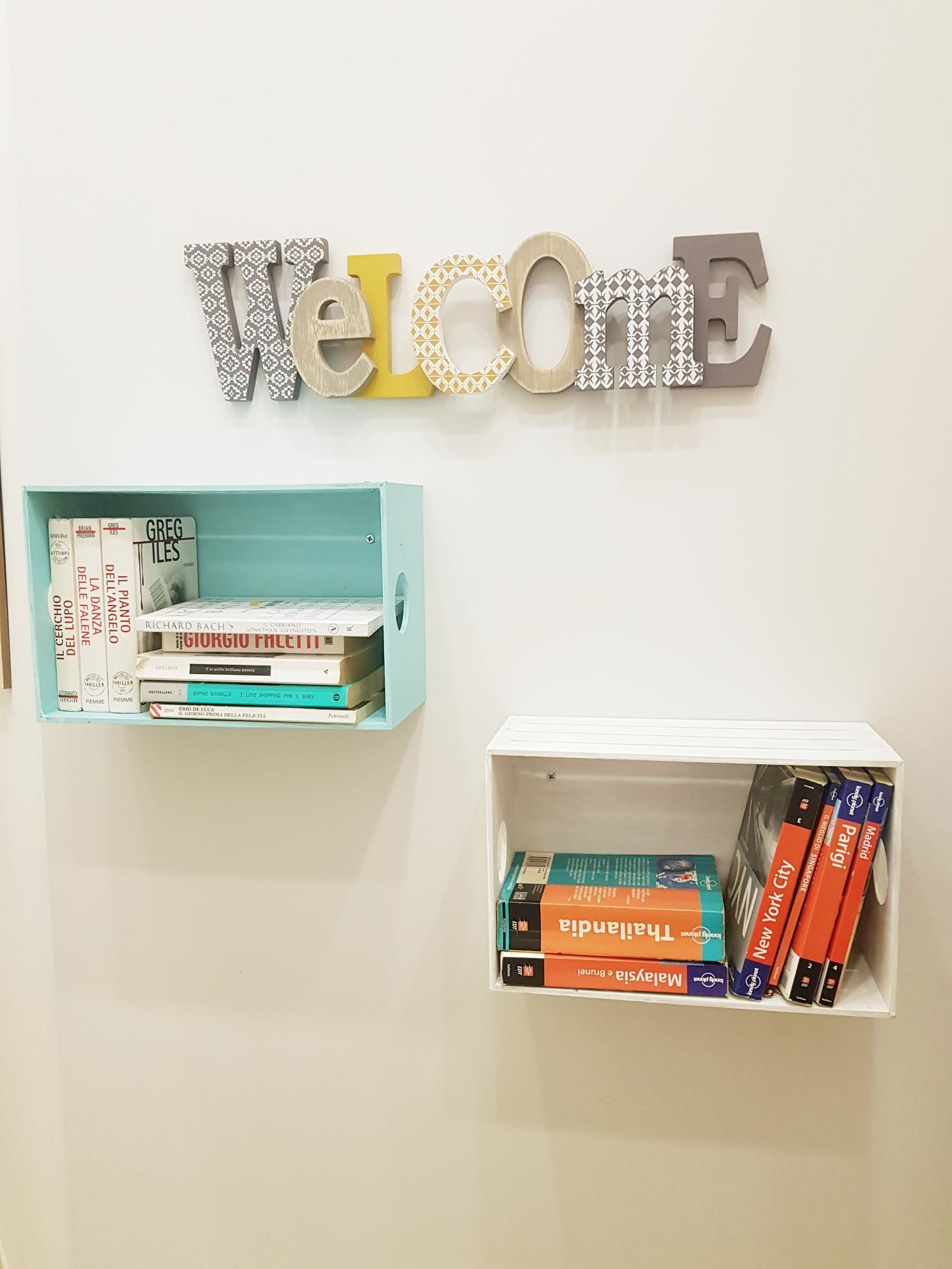 Un muro con un cartello che dice 'Welcome' e due mensole con libri.
