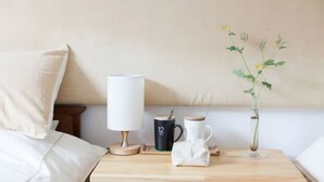 A neatly made bed with a pillow, a bedside table with a lamp, two mugs, and a vase with a plant. - Banshan Greatwall Mountain View Resort (Huairou)