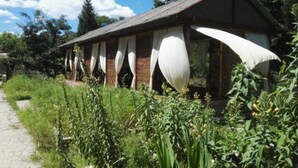 A rustic wooden building with large white curtains, surrounded by lush greenery and a clear sky. - Banshan Greatwall Mountain View Resort (Huairou)