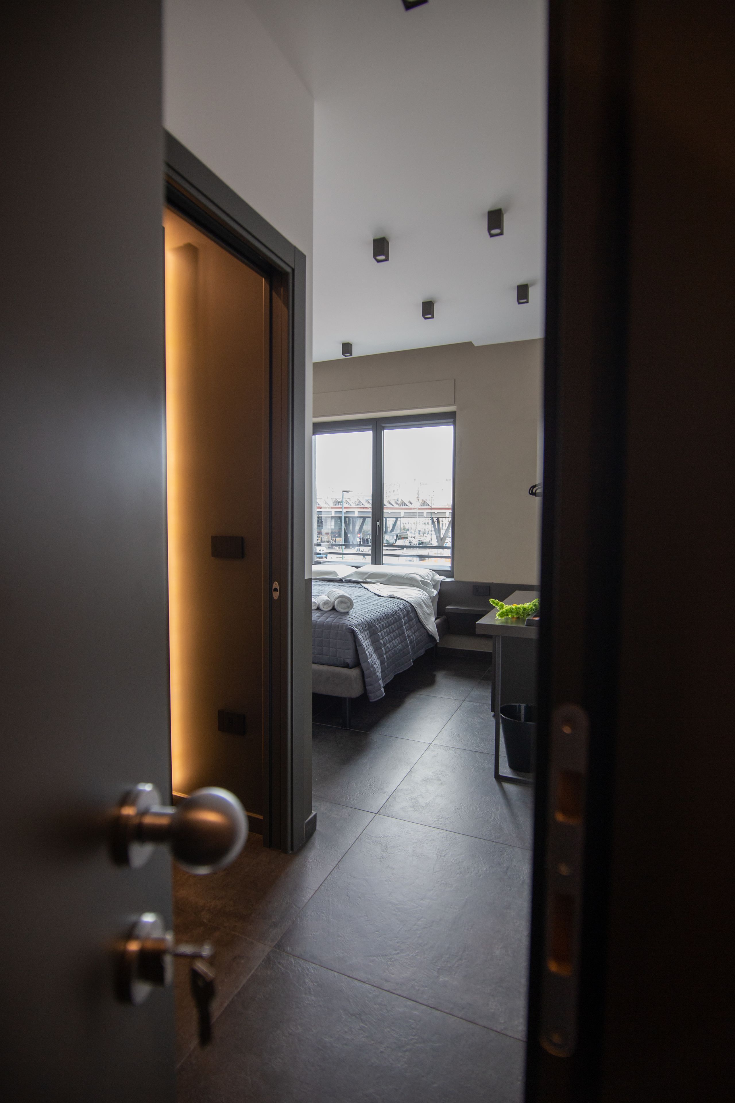 Una camera d'albergo moderna con una grande finestra, un letto, una scrivania e vista sulla città.