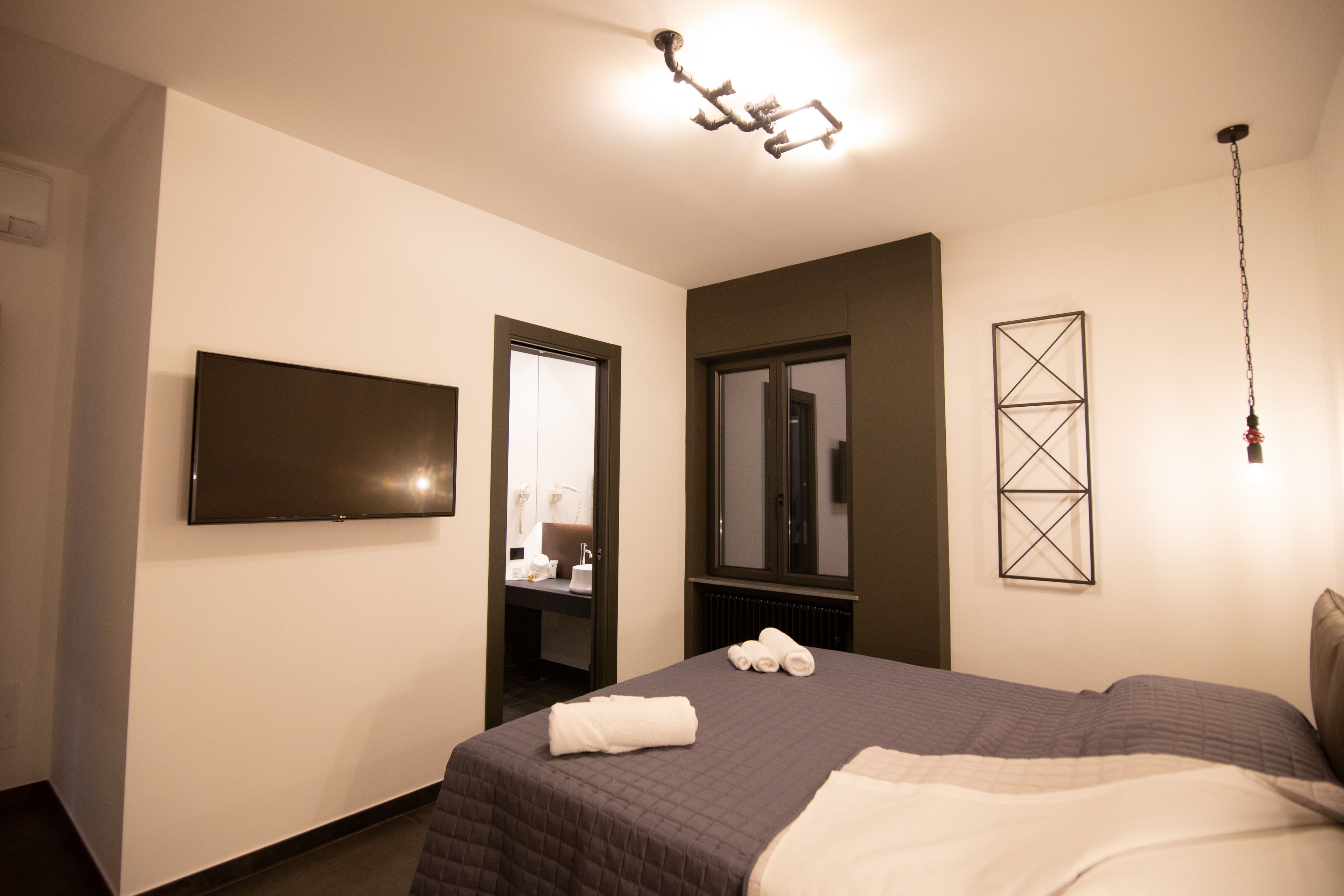 Ein Hotelzimmer mit einem Bett, einem an der Wand befestigten Flachbildfernseher, einem Spiegel und einem gerahmten geometrischen Kunstwerk.