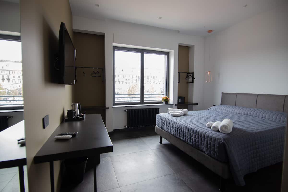 Ett modernt hotellrum med en stor säng, ett skrivbord, en platt-TV och ett fönster med utsikt över staden.