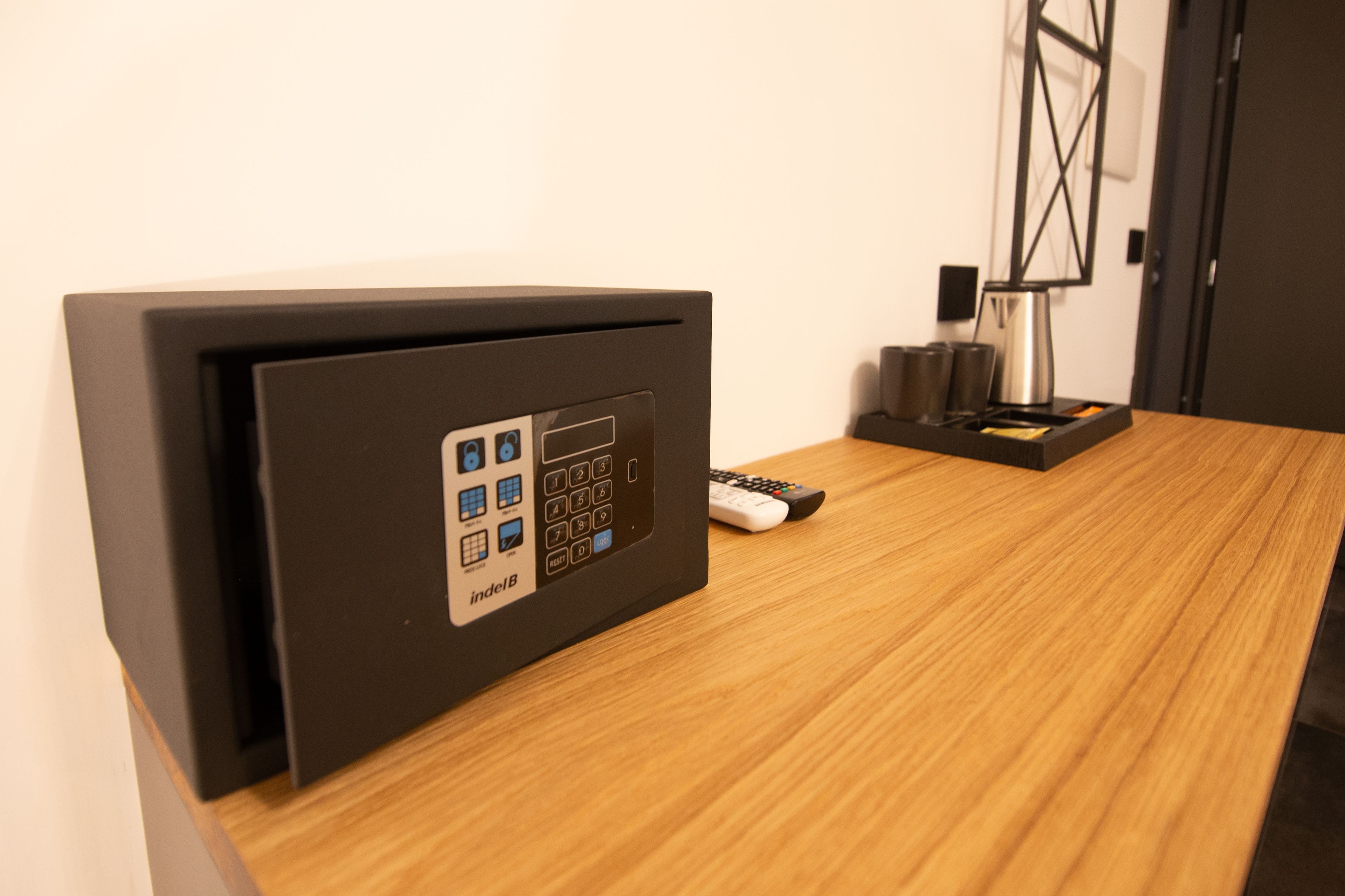 Un mini-bar noir doté d’un panneau de commande, d’une télécommande et d’une machine à café, le tout posé sur une table en bois.