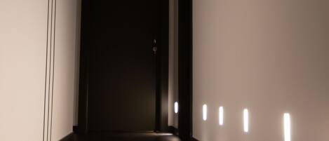 Un couloir au sol sombre, aux murs blancs, et une porte au fond.