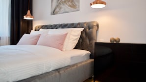 A modern bedroom with a tufted headboard, a large bed with white and pink bedding, two pendant lights, a dark nightstand, and a minimalist abstract painting on the wall. -  Apartament Nowe Miasto - Skwer Malarzy (Gorzow Wielkopolski)