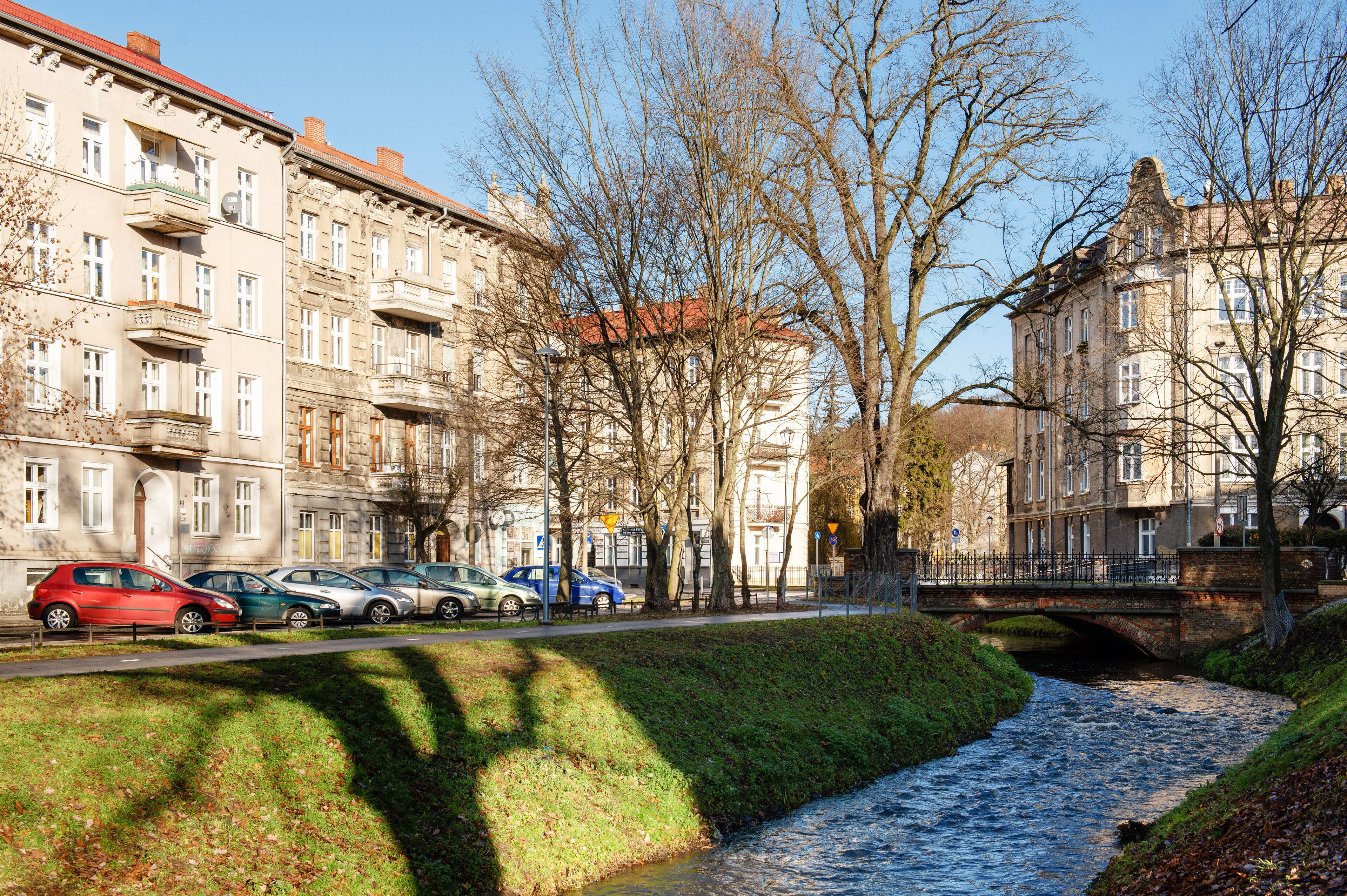 Une rivière traverse une ville où l’on trouve des bâtiments historiques et des voitures garées le long des berges.