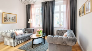 A living room with two grey sofas, a round coffee table, a chandelier, and a window with curtains. -  Apartament Nowe Miasto - Skwer Malarzy (Gorzow Wielkopolski)