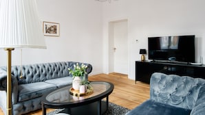 A modern living room with a tufted sofa, a round coffee table, a television, and a chandelier. -  Apartament Nowe Miasto - Skwer Malarzy (Gorzow Wielkopolski)