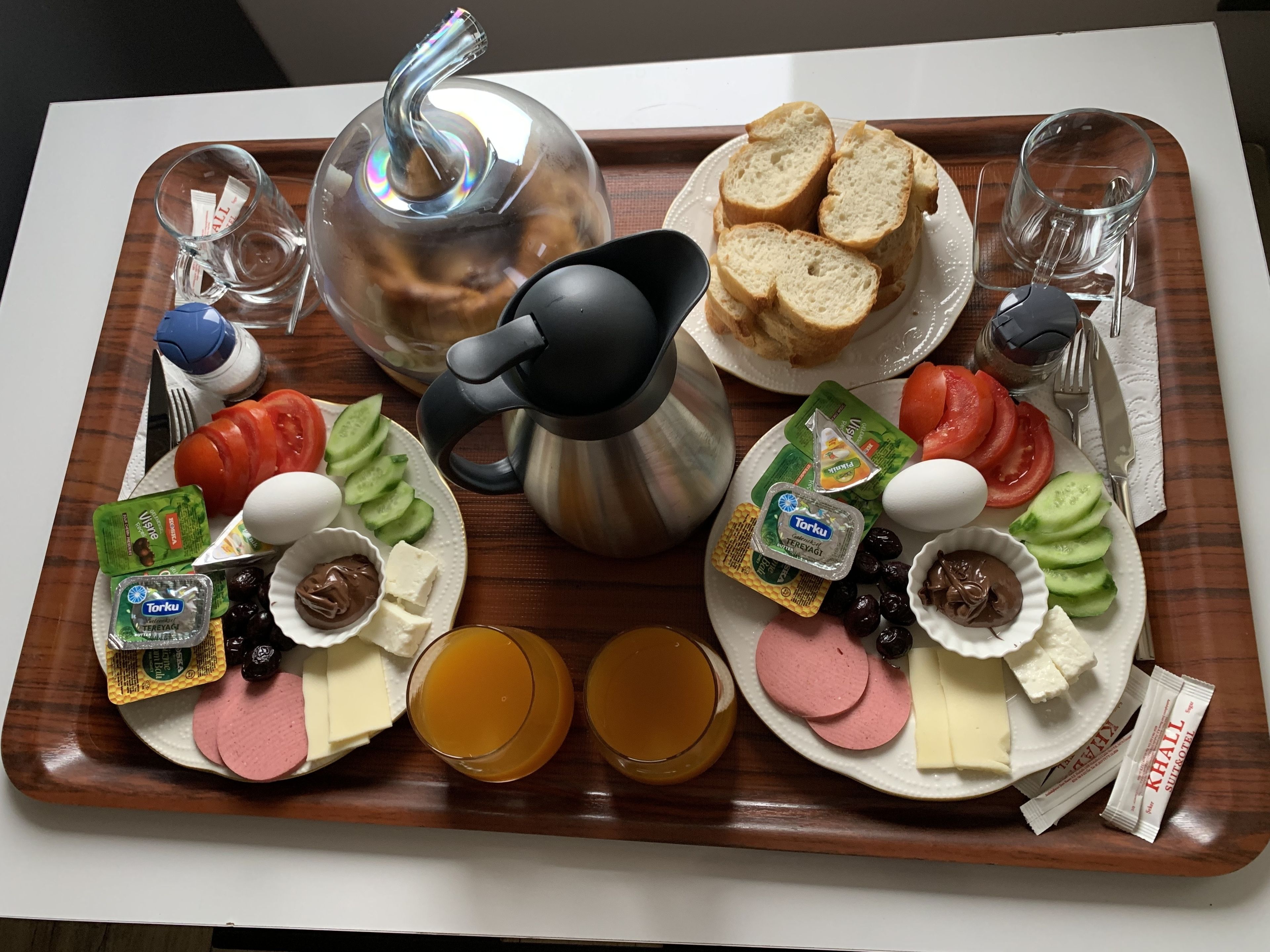 Bandeja de desayuno con pan, huevos, queso, tomates, pepinos, aceitunas y salsas.