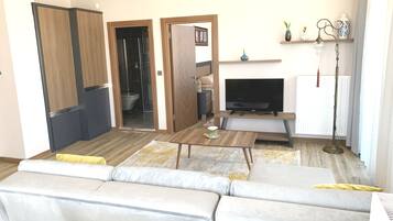 Un salon comprenant un canapé, une table basse, un téléviseur et une petite table ornée d’un objet décoratif.