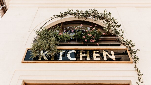 A building facade with a "KITCHEN" sign under an arched window, surrounded by greenery and potted plants. - Five Elements Luxury Rooms (Split)
