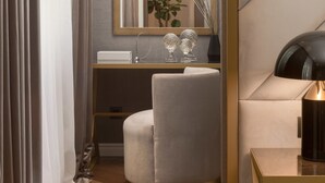 A modern room with a round grey sofa, a bedside table with a lamp, a mirror, and a plant on the dresser. - Five Elements Luxury Rooms (Split)