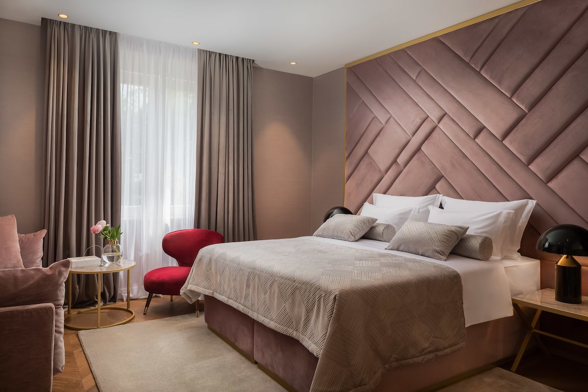 A modern bedroom with a large bed, a red chair, a small round table, and a nightstand with a lamp.