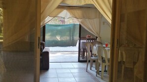 A sliding glass door leading to an outdoor patio area with a table and chairs, a covered seating area, and a view of a garden. -  Las Quintas Casas para Vacacionar (Sardinal)
