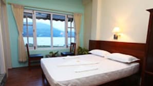 A bedroom with a bed, a chair, a window with a view, and a bedside lamp. - The Lake House (Pokhara)