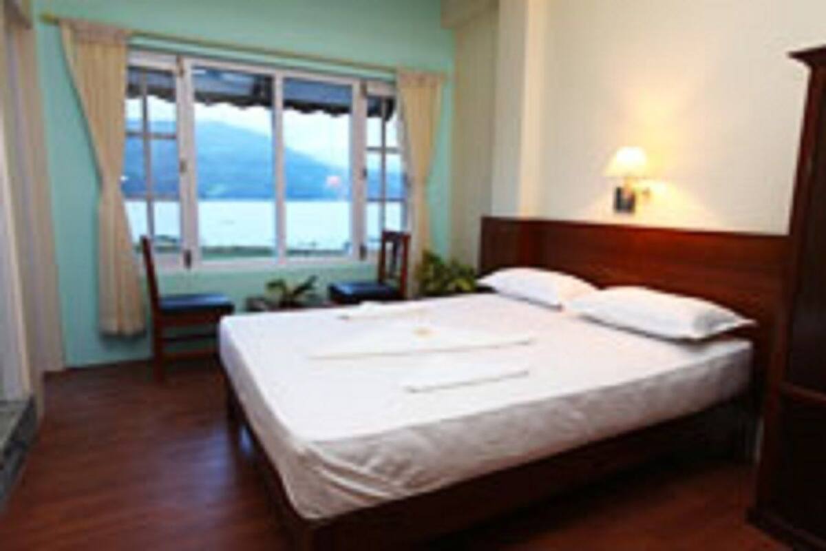 A bedroom with a bed, a chair, a window with a view, and a bedside lamp.