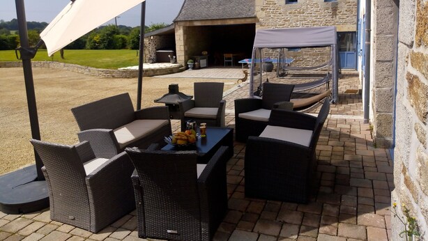Ein Patio im Freien mit Korbmöbeln und einem Tisch, ein Steinhaus im Hintergrund sowie eine überdachte Sitzgelegenheit.