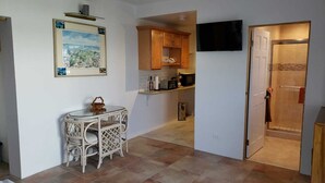 A compact kitchen with wooden cabinets, a small dining table, and a TV mounted on the wall. - Paul's Oceanview Apartment with Amazing Sunsets + Twizy Charger (Sandy's)