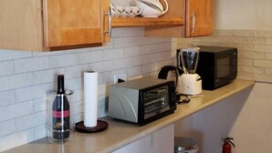 A kitchen with wooden cabinets, a microwave, a blender, and a fire extinguisher. - Paul's Oceanview Apartment with Amazing Sunsets + Twizy Charger (Sandy's)