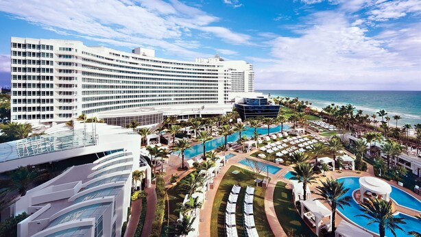 Un resort con varias piscinas, un gran edificio de hotel y vista al mar.