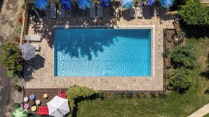 An aerial view of a rectangular swimming pool surrounded by lounge chairs and umbrellas, with a paved deck and greenery. - Gite La Tour - Cocoon for 2 with pool and nature (Saint-Geyrac)
