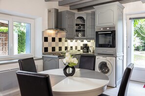A modern kitchen with grey cabinetry, a built-in oven, a washing machine, and a dining area with a round table and chairs.