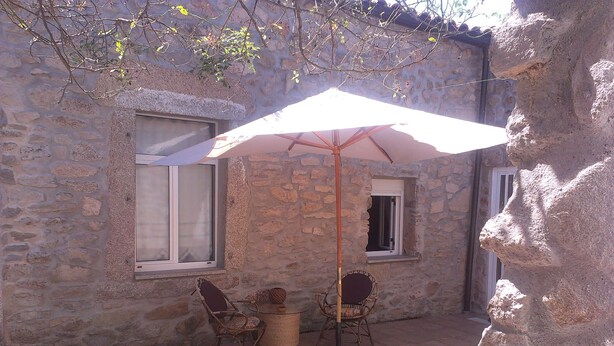 A stone building with a patio area featuring two wicker chairs and a table under a white umbrella. - El Condado Casa Rural (Fuentes de Onoro)