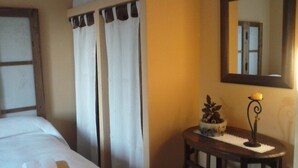 A hotel room with a bed, curtains, a small table with a candle, and a mirror on the wall. - El Condado Casa Rural (Fuentes de Onoro)