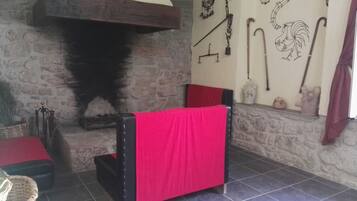 Una habitación rústica con chimenea de piedra, una silla roja y varias herramientas y adornos en la pared.