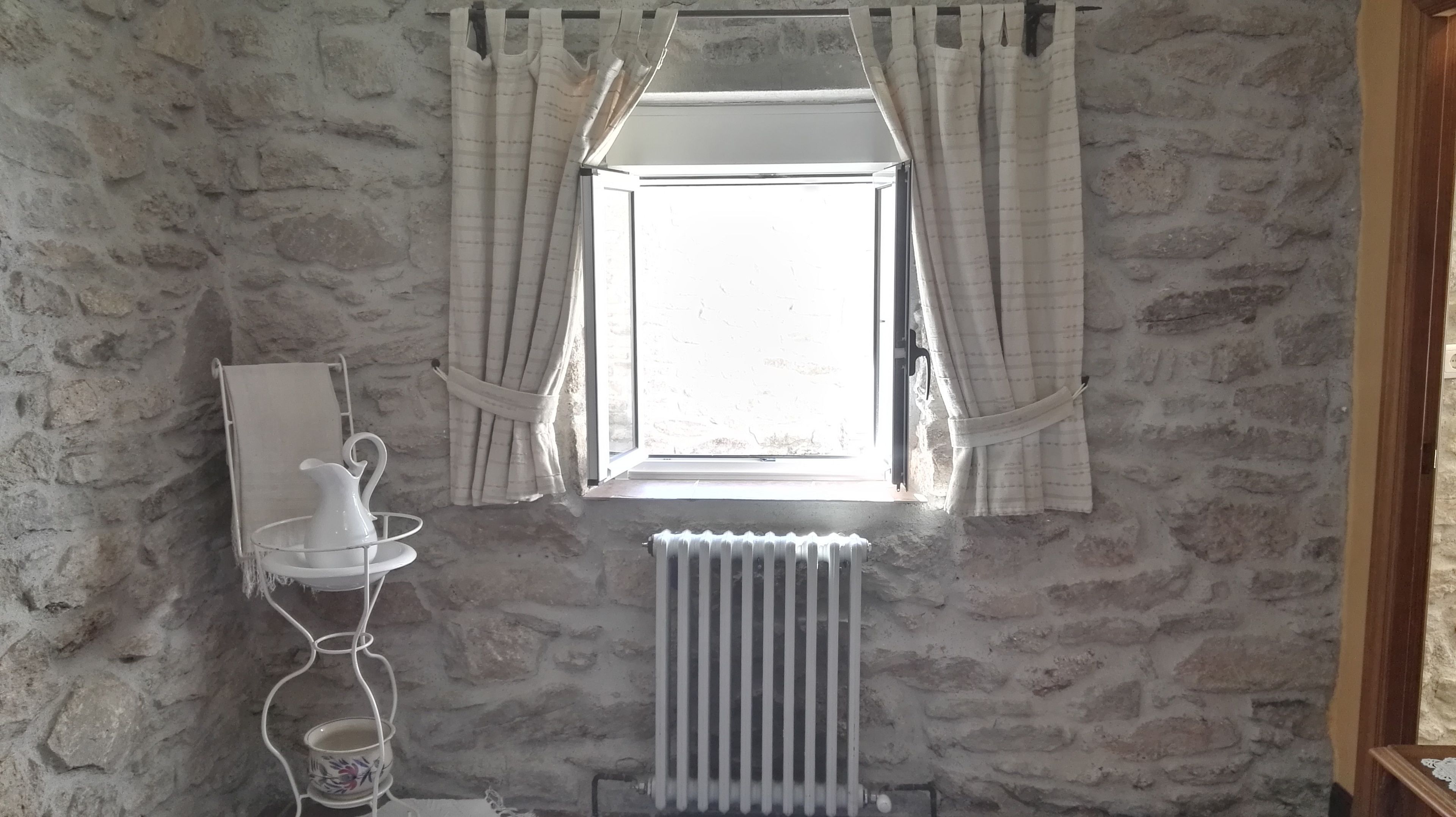 A room with a stone wall, a radiator, a window with curtains, and a small table with a pitcher and cups.