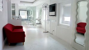 A modern hotel room with a red sofa, a large mirror, and a TV on the wall. - Hospedería Diez y Seis (Tarifa)