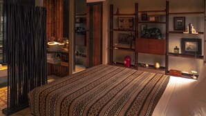 A bedroom with a patterned bedspread, a wooden wardrobe, and a shelf with decorative items. - Hospedería Diez y Seis (Tarifa)