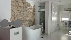 A modern bathroom with a stone wall, a freestanding bathtub, and a glass shower enclosure. - Hospedería Diez y Seis (Tarifa)