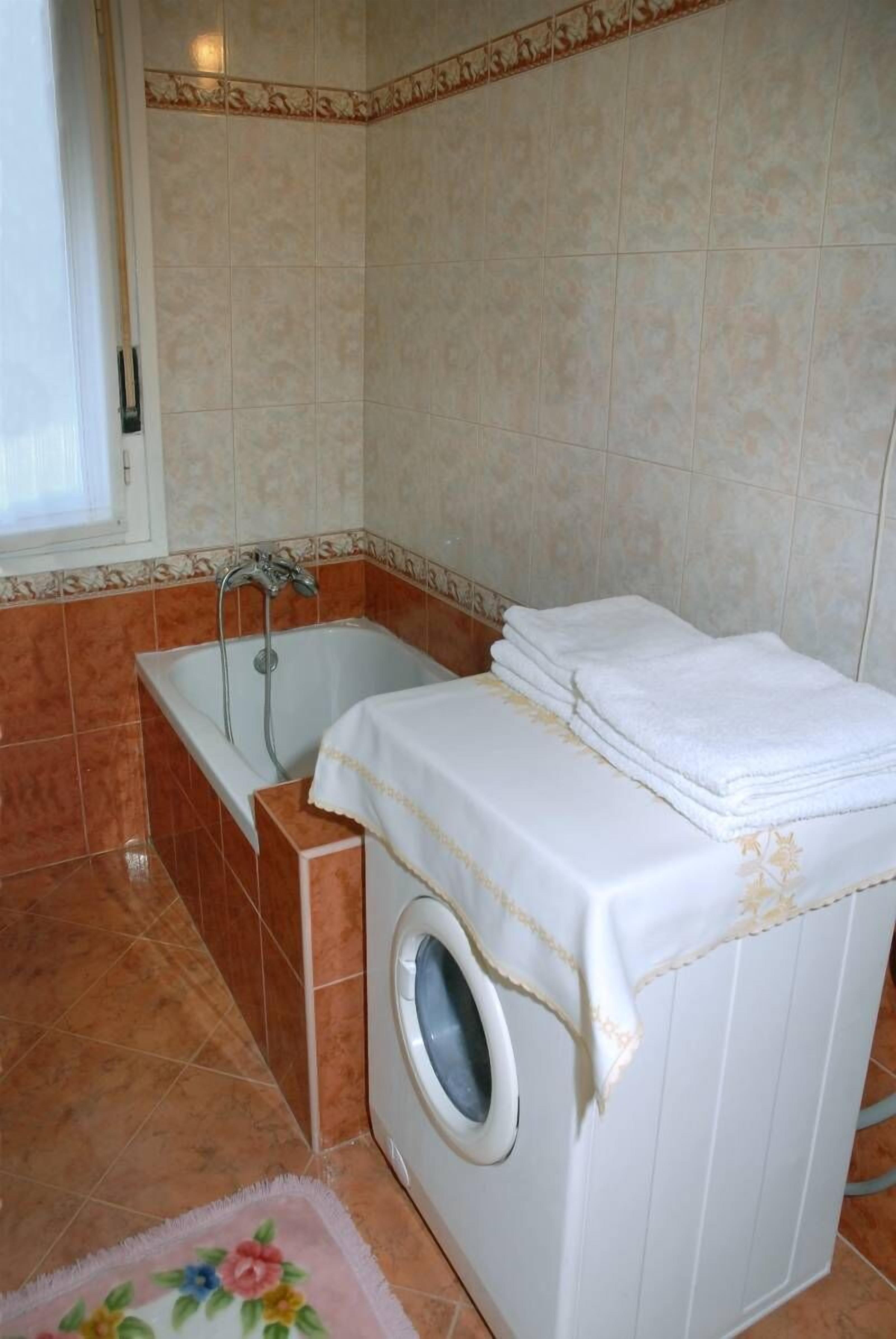 A bathroom with a bathtub, a washing machine, and a tiled floor.