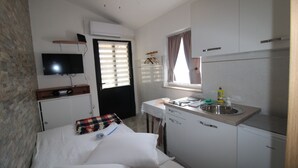 A compact hotel room with a bed, a small desk, a television, a kitchenette, and a window with curtains. - House Marija (Pula)