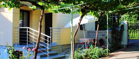 A residential building with a staircase leading to a door, a small garden area with plants and flowers, and a metal railing.