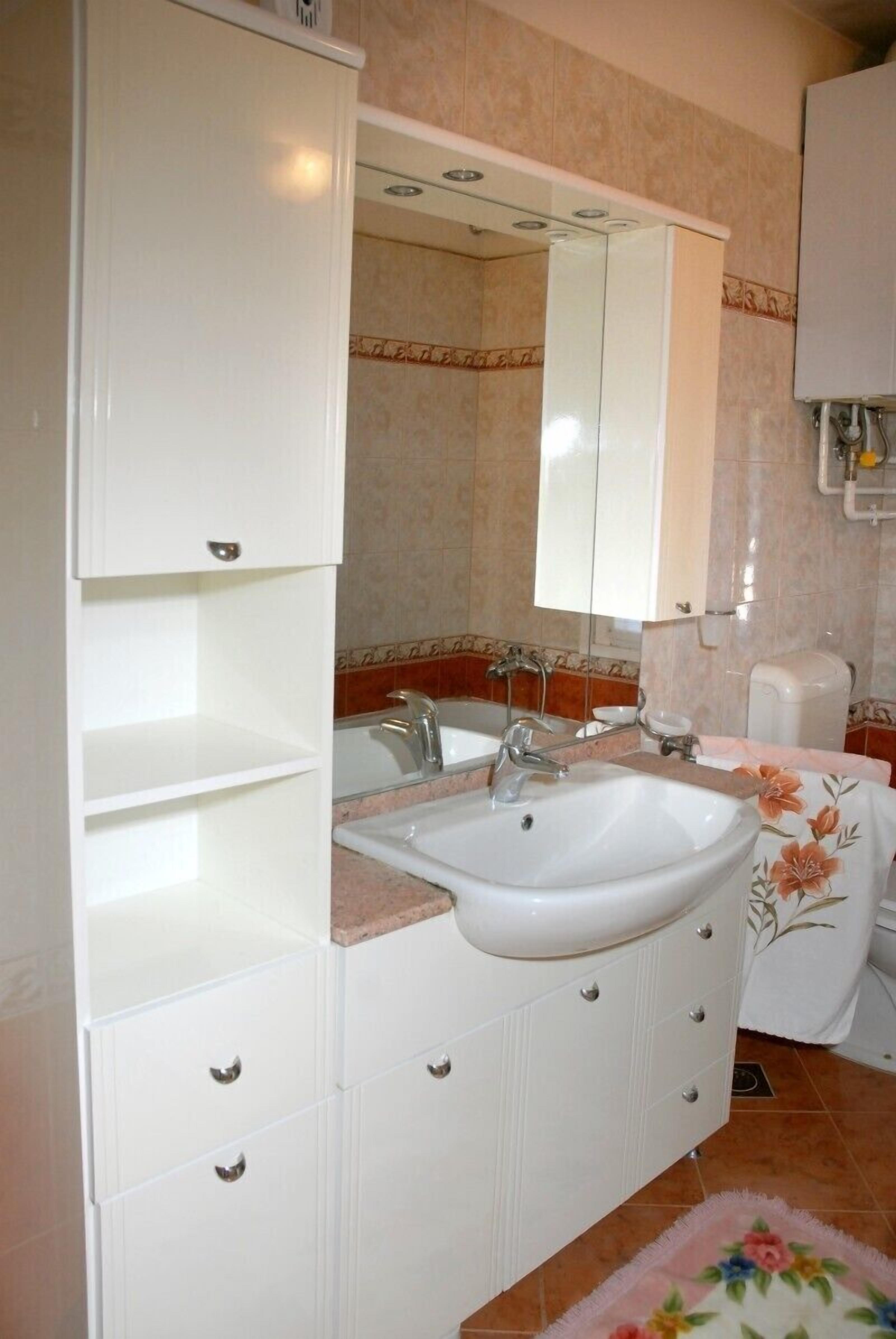 A bathroom with a white sink, mirror, and cabinet, a shower area, and a floral rug.