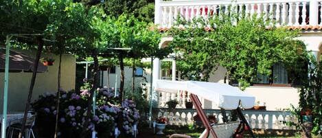 Un jardín con una silla mecedora, una pérgola y un edificio con balcón.