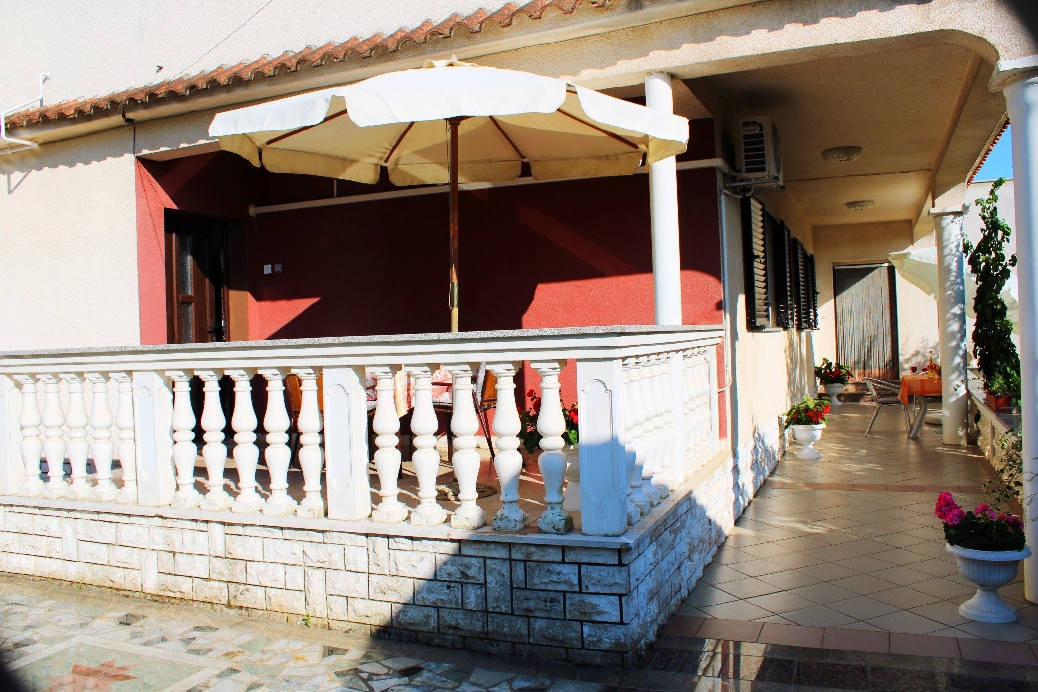 A building with a covered porch, white balustrades, and potted plants.