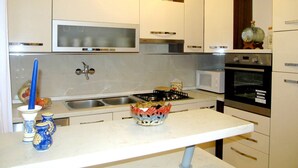 A modern kitchen with white cabinets, a stainless steel sink, a microwave, and an oven. - House Marija (Pula)