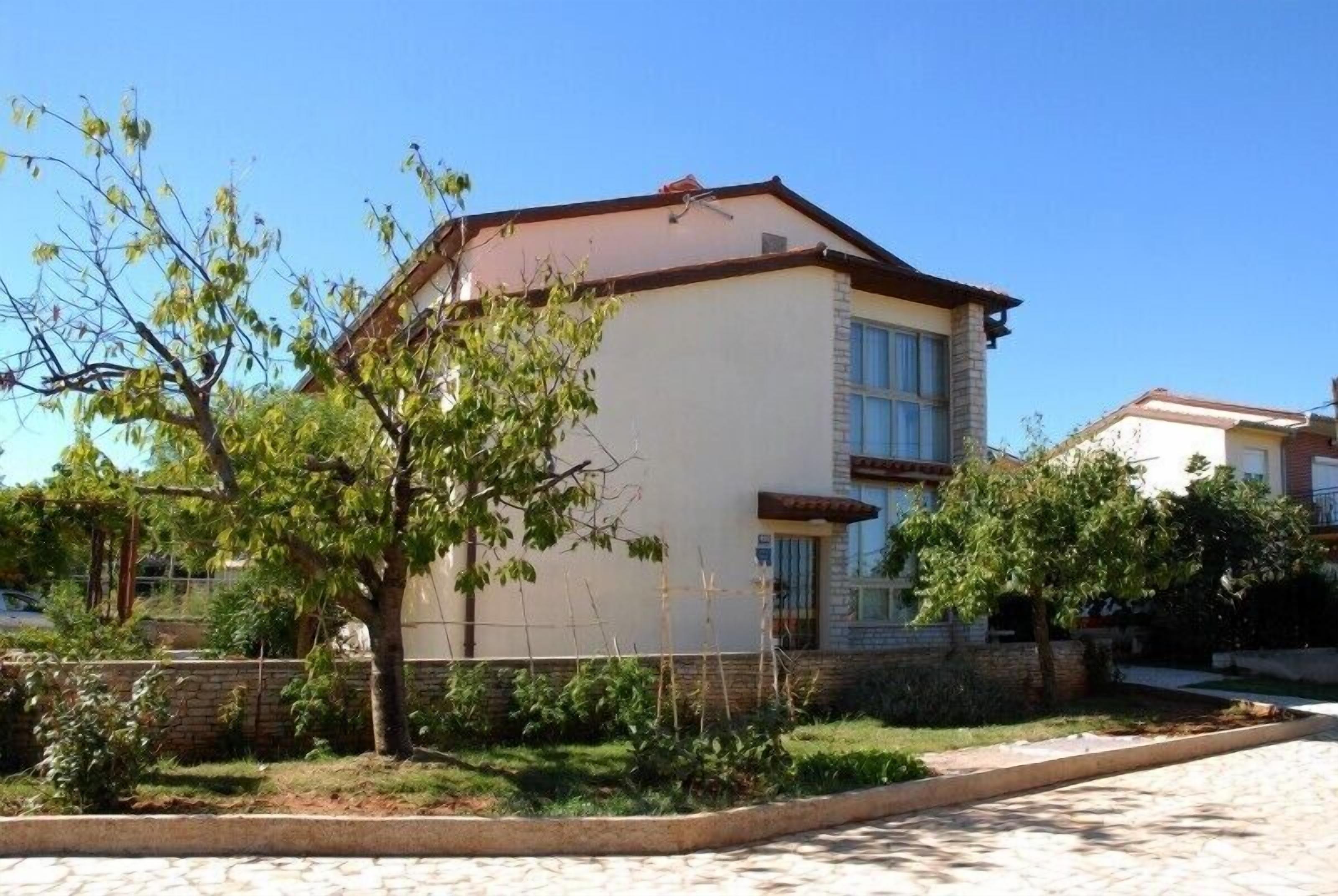A two-story house with a flat roof, a visible window, and a garden in front.