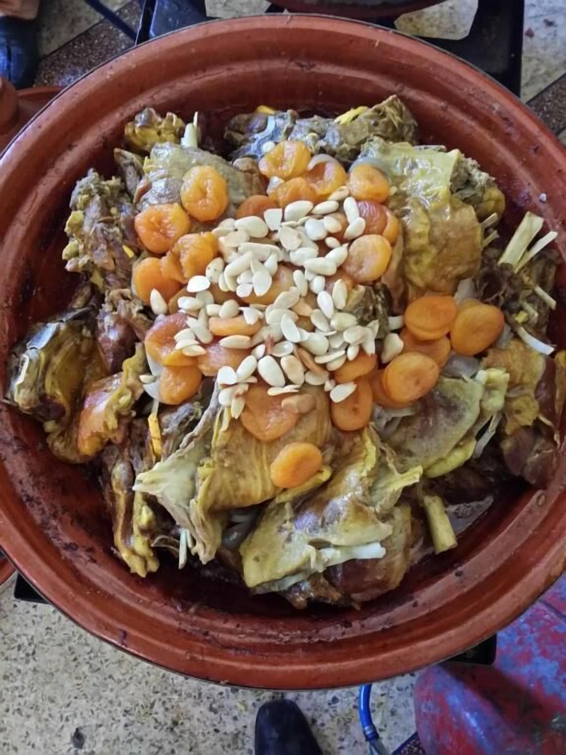Uma grande panela de barro cheia de um ensopado, decorada com amêndoas e cenouras.
