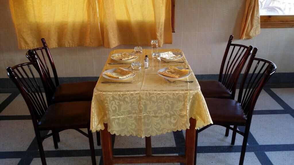 Mesa de comedor preparada para cuatro, con mantel, platos, cubiertos y saleros y pimenteros.