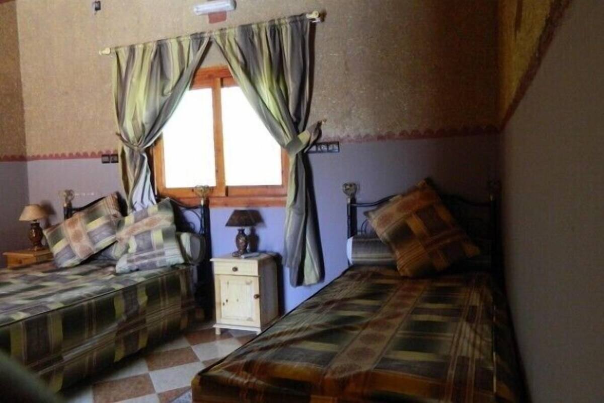 Een slaapkamer met twee bedden, een raam met gordijnen, een nachtkastje en een lamp.